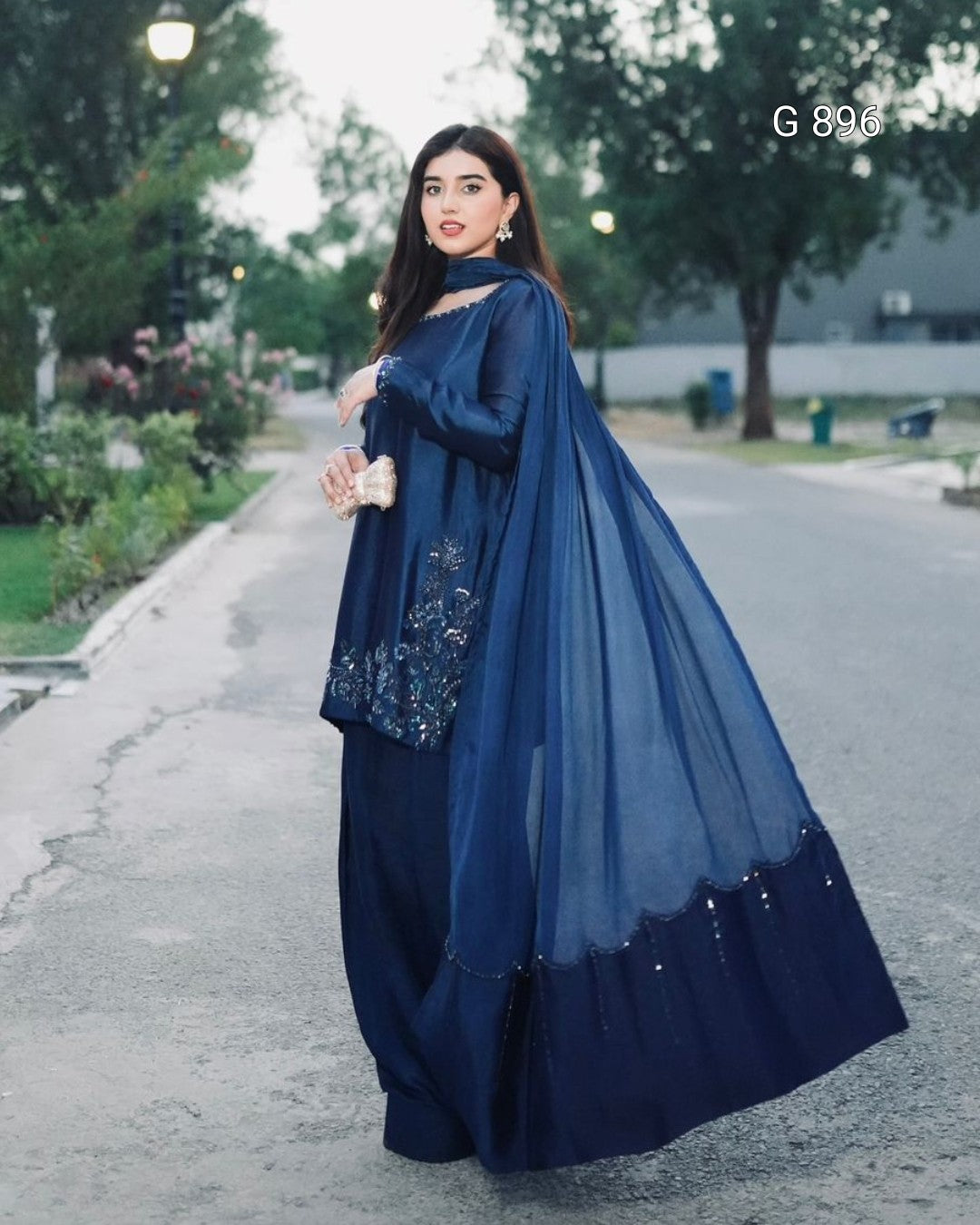 Woman in a blue traditional outfit standing on a road with trees in the background