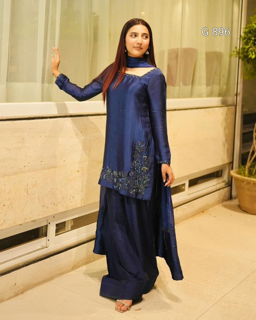 Woman wearing a blue traditional outfit with intricate designs, standing indoors.