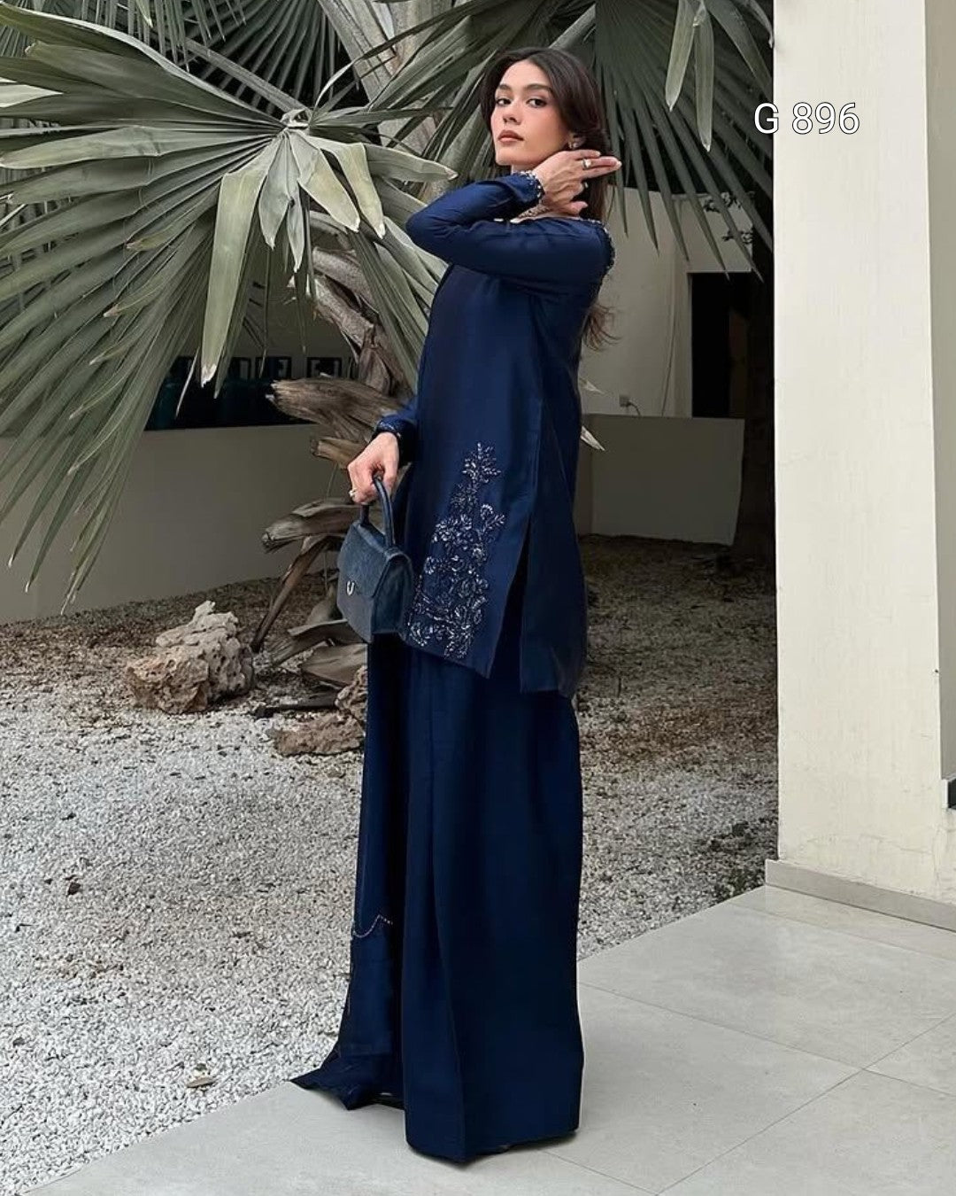 Woman in a blue outfit standing outdoors with plants in the background