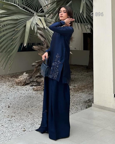 Woman in a blue outfit standing outdoors with plants in the background