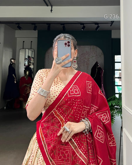 Person wearing a red and beige saree with jewelry in a mirror selfie.