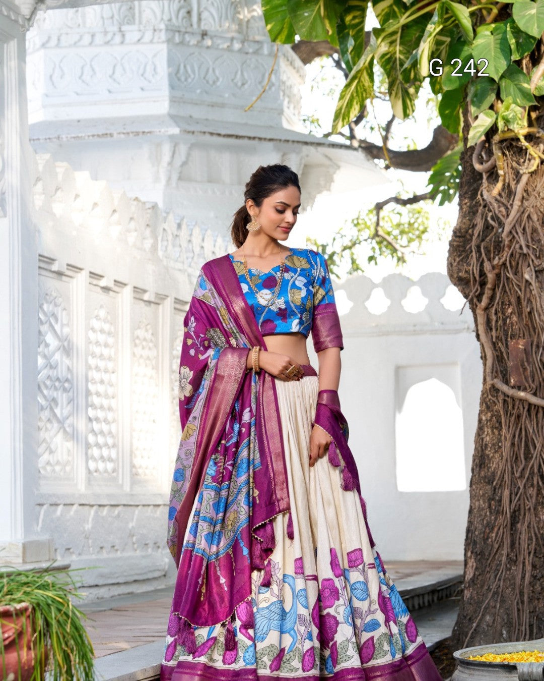 Woman in a colorful traditional outfit standing in a decorative setting with plants.