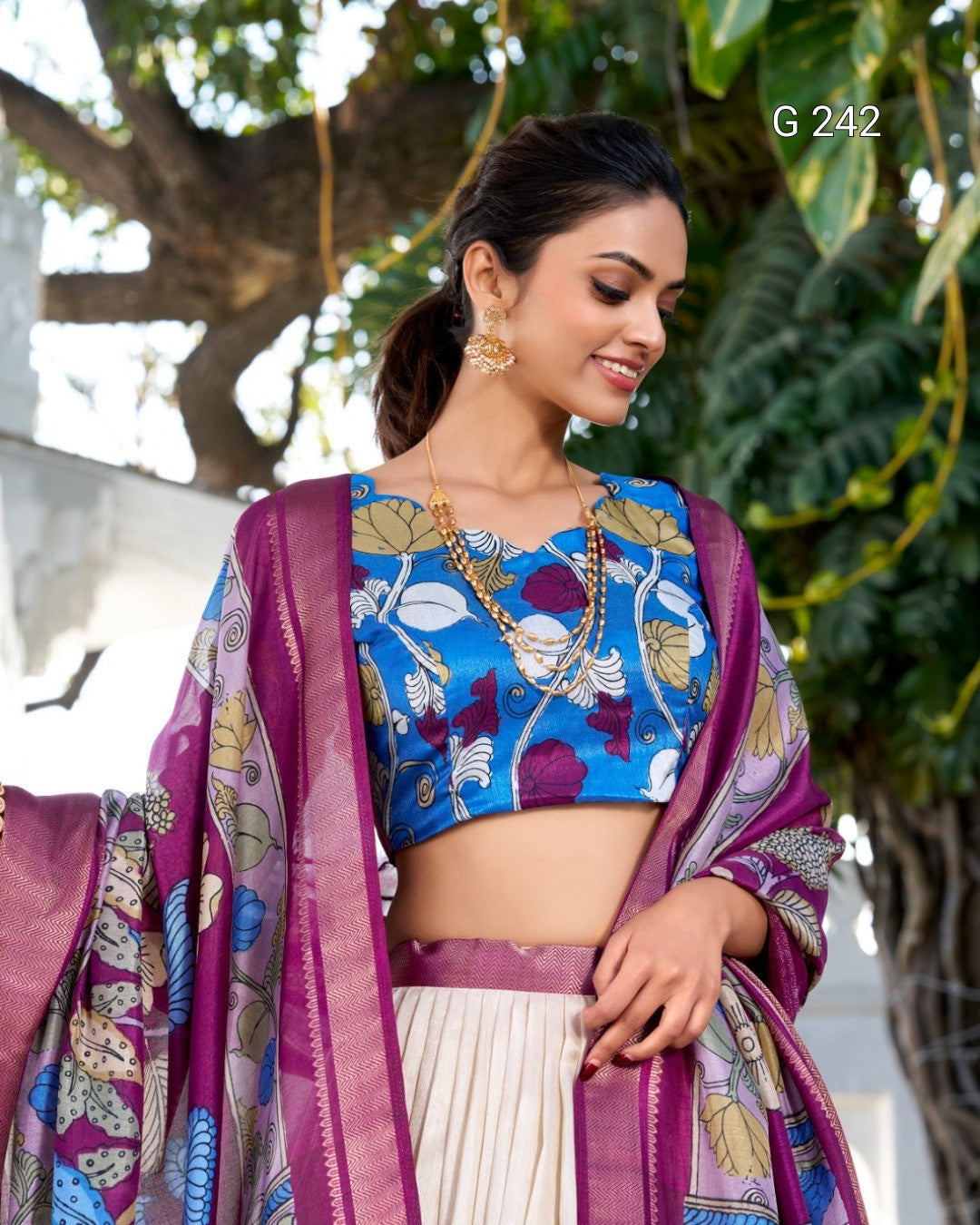 Woman wearing a traditional outfit with a blue blouse and purple dupatta in an outdoor setting.