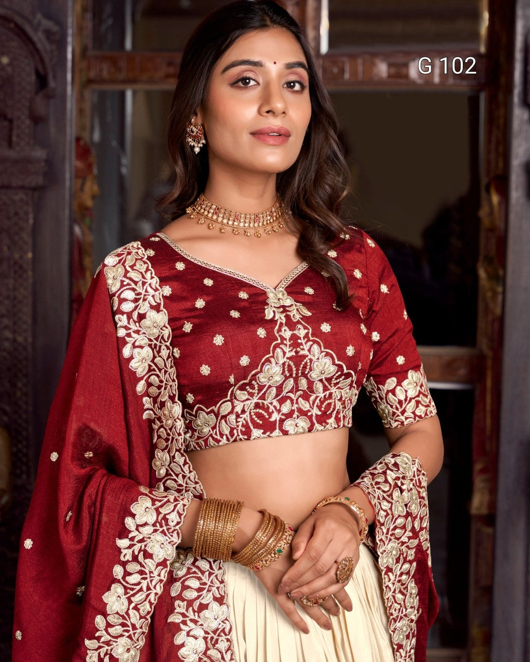 Woman wearing a traditional maroon and gold saree with jewelry indoors.