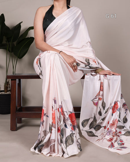 Woman wearing a white saree with floral patterns, sitting on a chair.