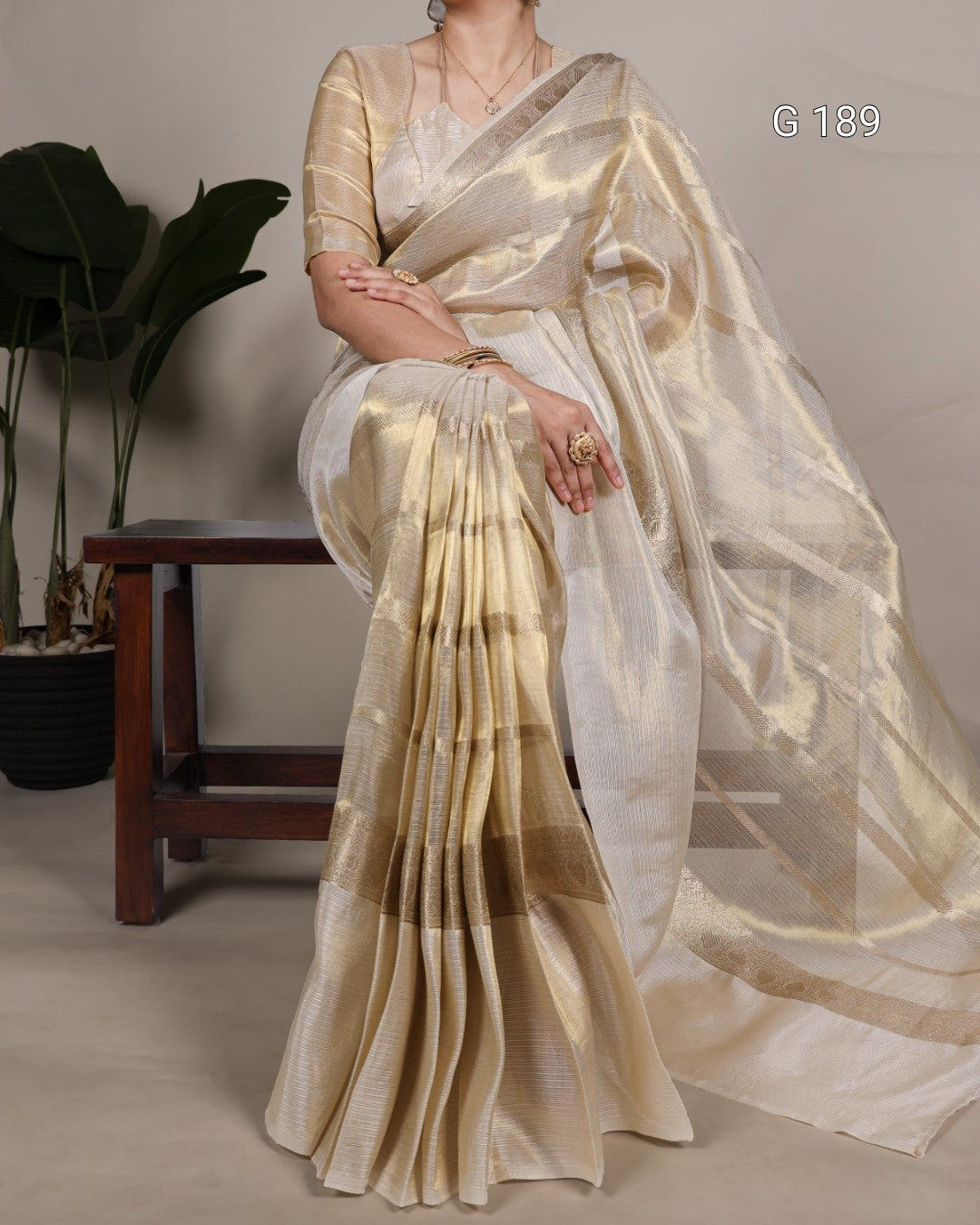 Woman wearing a beige saree with a subtle pattern, sitting against a neutral background.