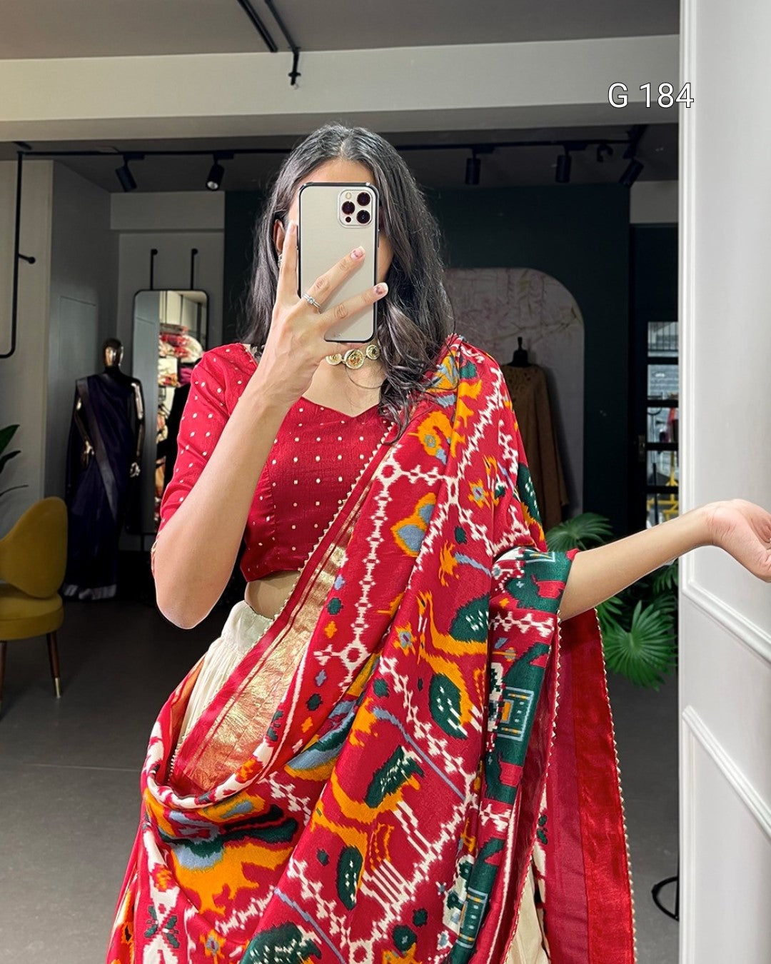 Person wearing a red saree with colorful patterns in an indoor setting.