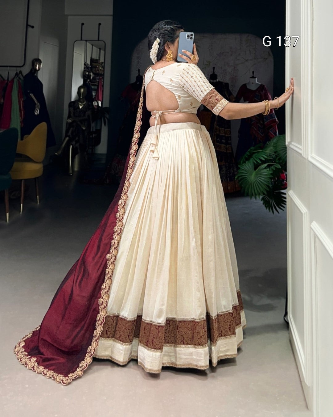 Woman taking a mirror selfie wearing a traditional outfit with a white saree and maroon blouse.