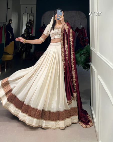 Person wearing a traditional outfit with a white and brown dress and maroon dupatta in a room.