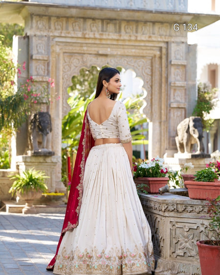Woman in a white traditional outfit with a red dupatta standing in front of an ornate stone structure.
