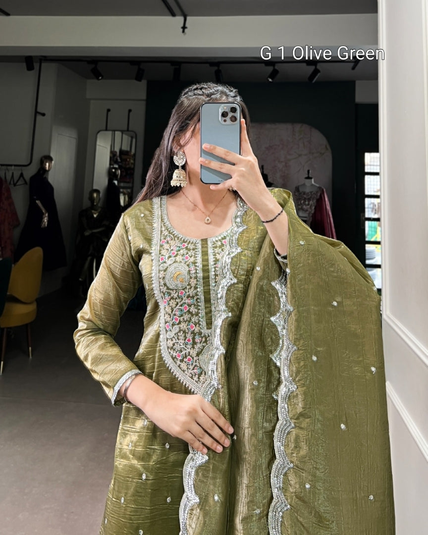 Person wearing an olive green traditional outfit with intricate white embroidery in a room.