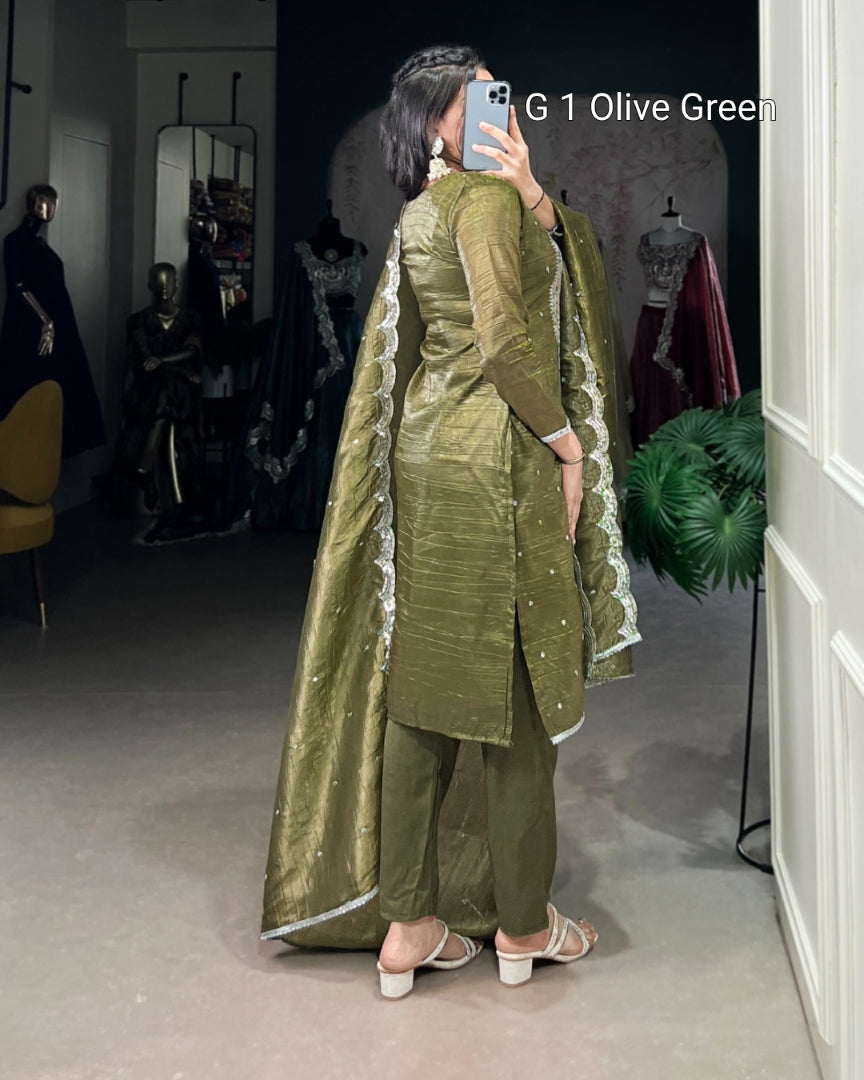 Person wearing an olive green traditional outfit with white lace details, standing in a room with mannequins and clothing.