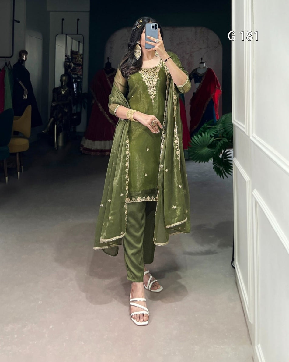 Person wearing a green traditional outfit with embroidery in a room with mirrors and clothing.