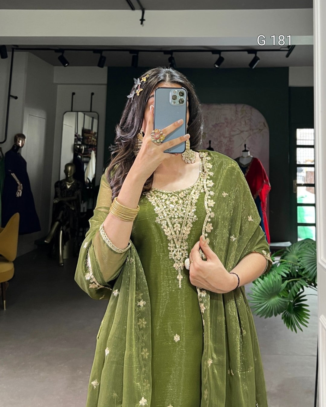 Person wearing a green traditional outfit with gold embroidery in a room.