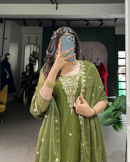 Person wearing a green traditional outfit with gold embroidery in a room.