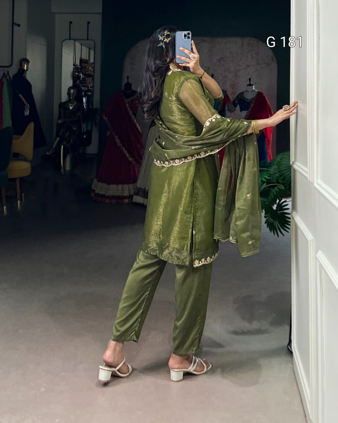 Person wearing a green traditional outfit taking a mirror selfie in a store.