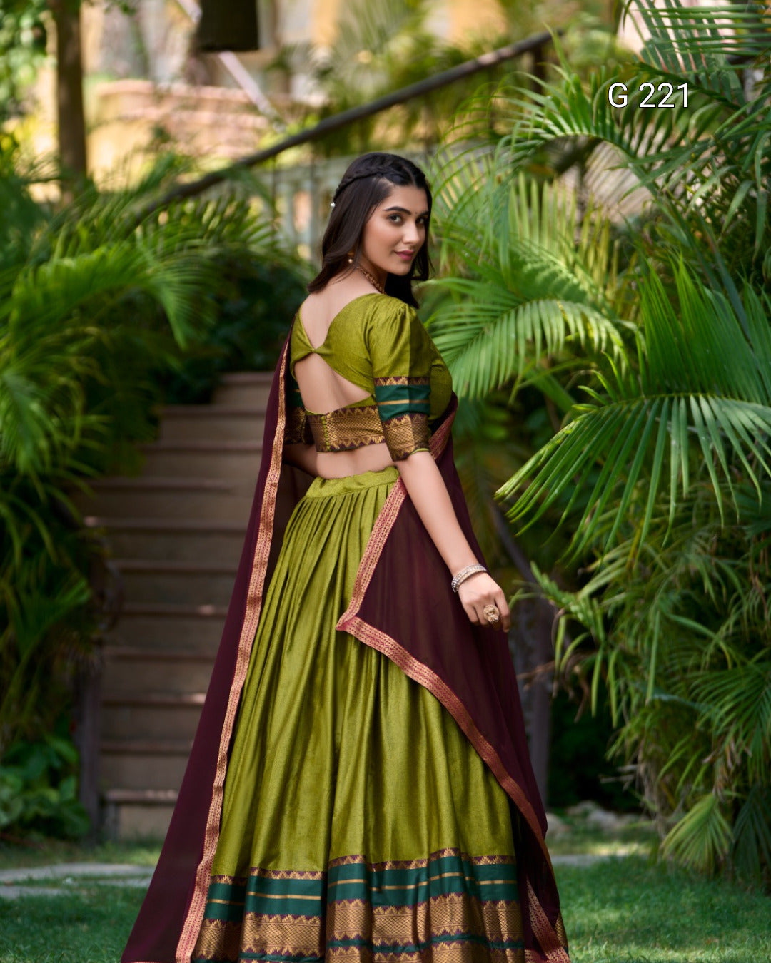 Woman in a green and brown traditional outfit standing in a garden.