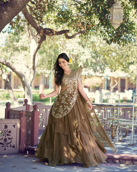 Woman in a brown and gold dress standing outdoors with trees and chairs in the background