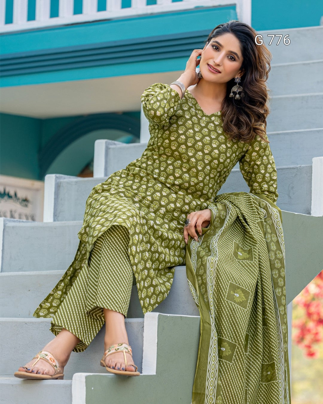 Woman in a green patterned outfit sitting on steps with a blurred background