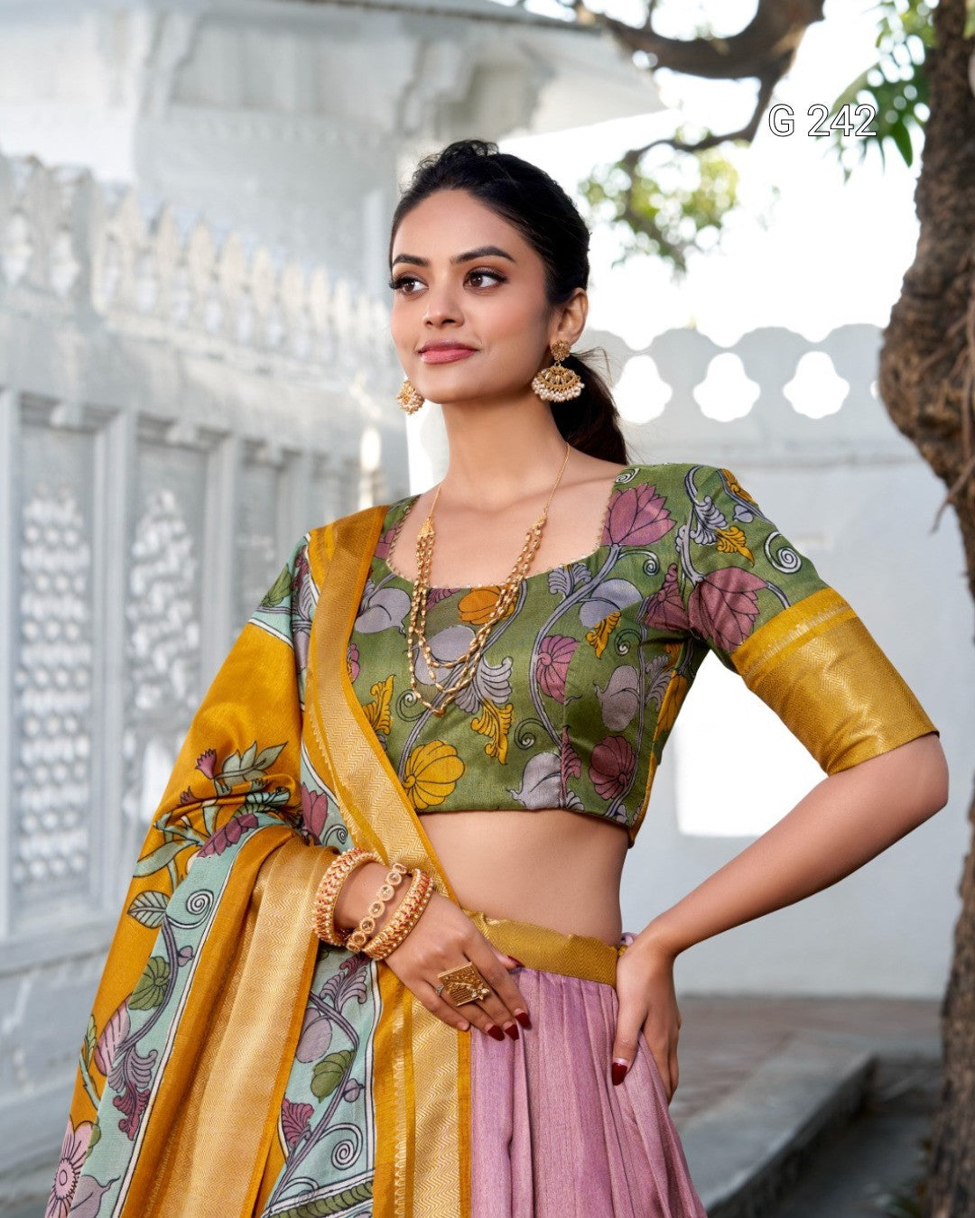 Woman wearing a traditional outfit with a floral blouse and yellow dupatta in an outdoor setting.
