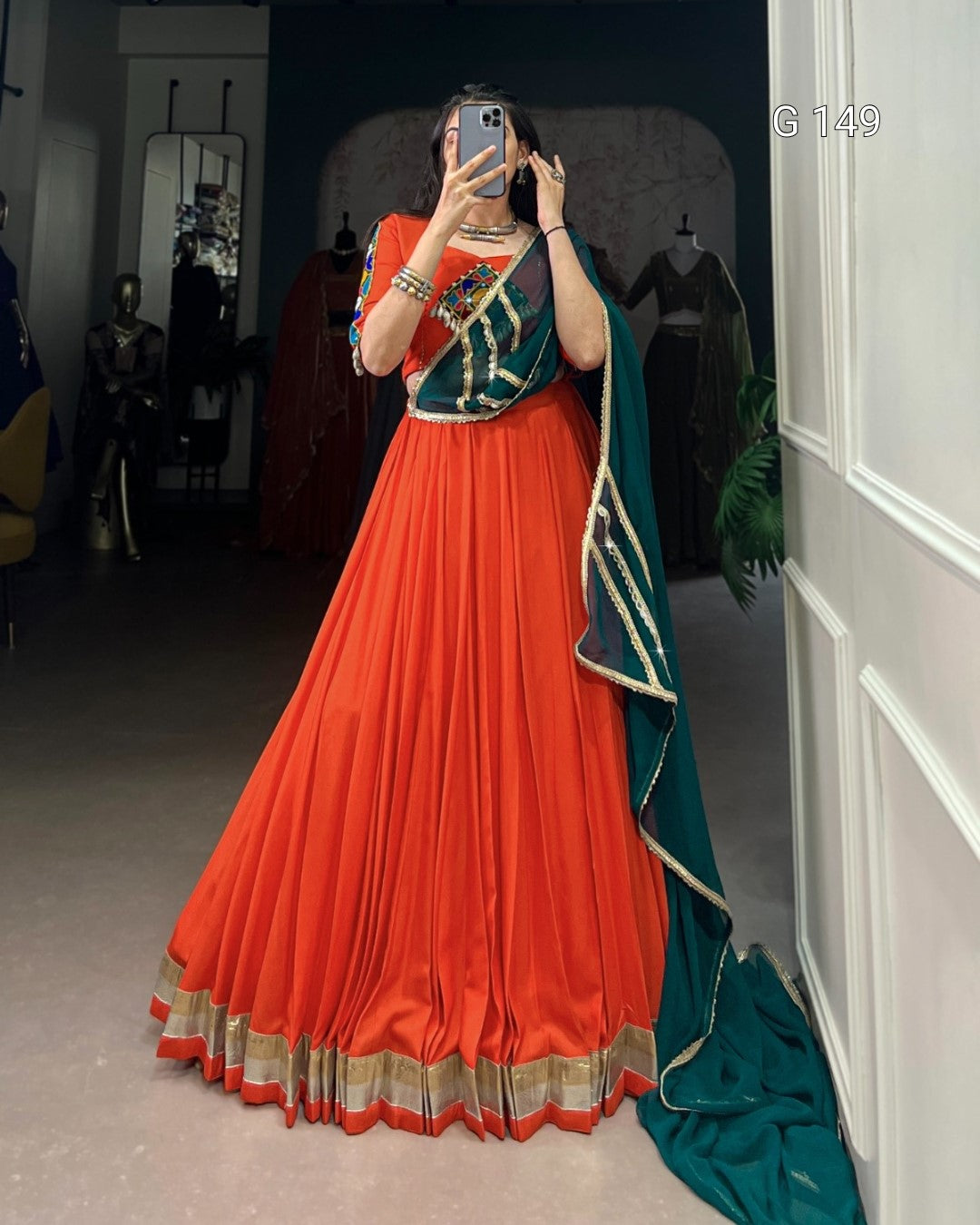 Person wearing a traditional orange and green outfit with a matching dupatta, standing indoors.