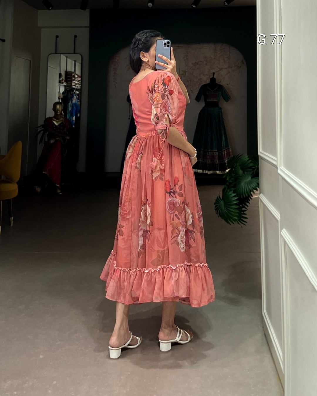 Person wearing a pink floral dress taking a mirror selfie in a room.