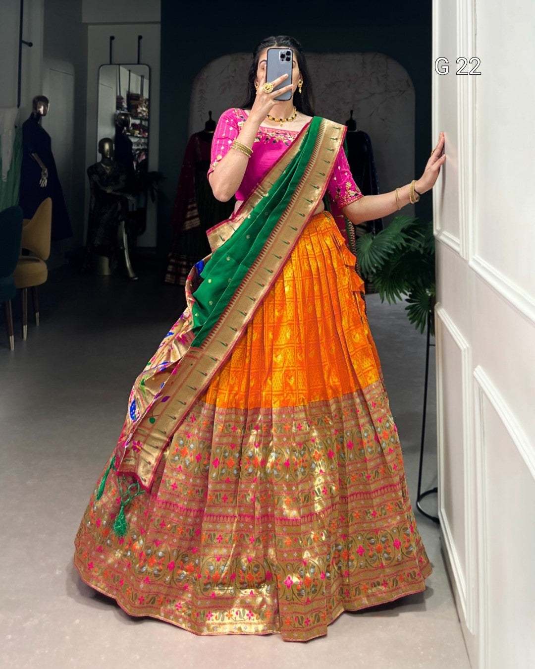Person wearing a traditional orange and green saree with a pink blouse, standing in a room.