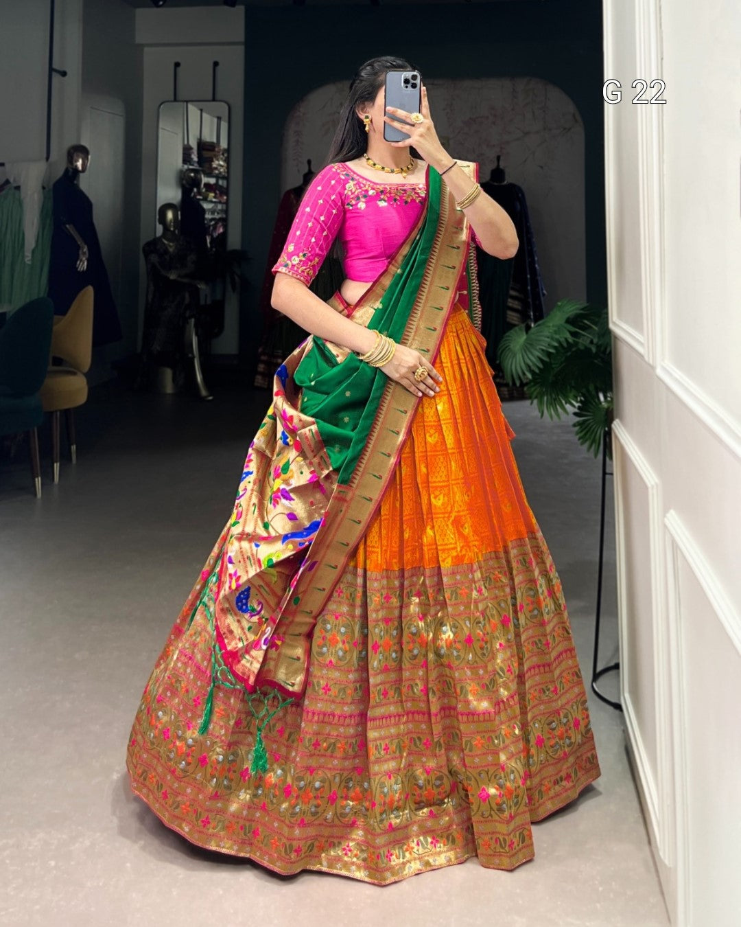 Person wearing a colorful traditional outfit with an orange and green saree in a room.