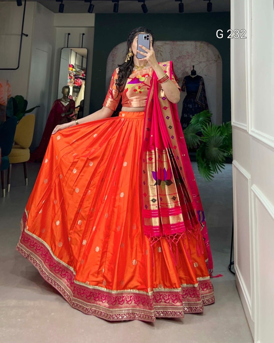 Person wearing a traditional orange and red saree with gold patterns in a room.
