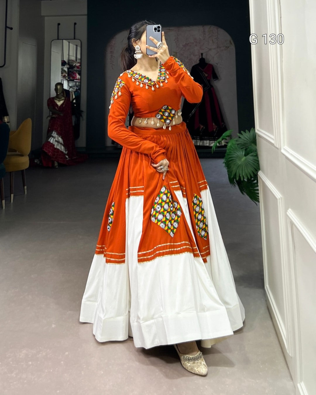 Woman taking a mirror selfie wearing an orange and white traditional outfit with intricate designs.