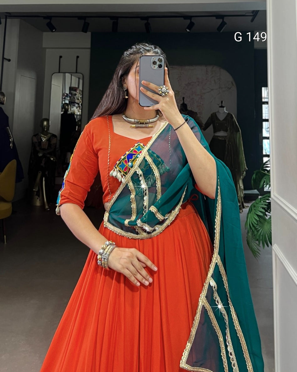Woman taking a mirror selfie wearing an orange and green traditional outfit with intricate designs.