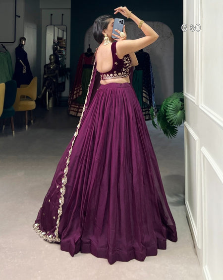 Person wearing a purple traditional outfit with intricate designs, standing in a room with mirrors and furniture.