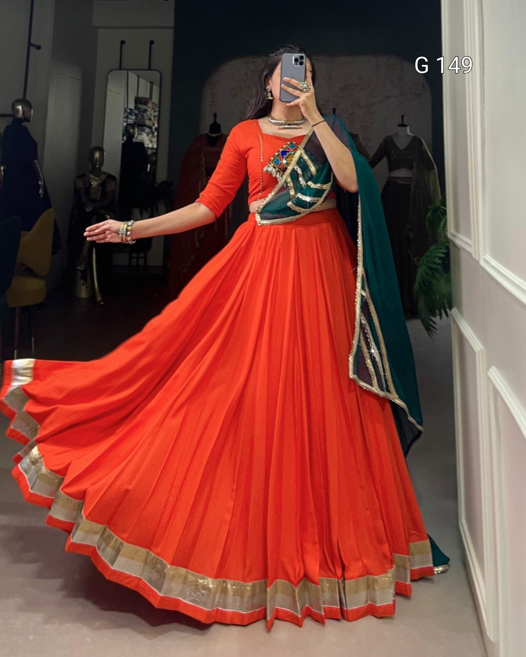 Person wearing a bright orange saree with a green blouse in a room.