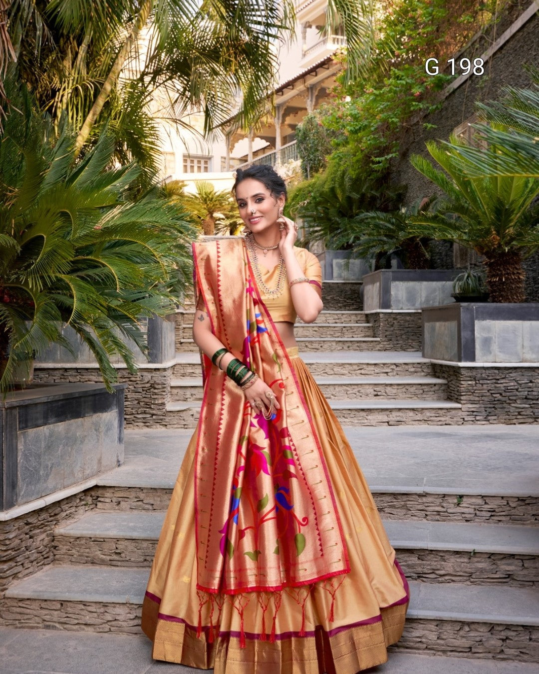 Woman in a traditional saree standing outdoors with plants and steps in the background