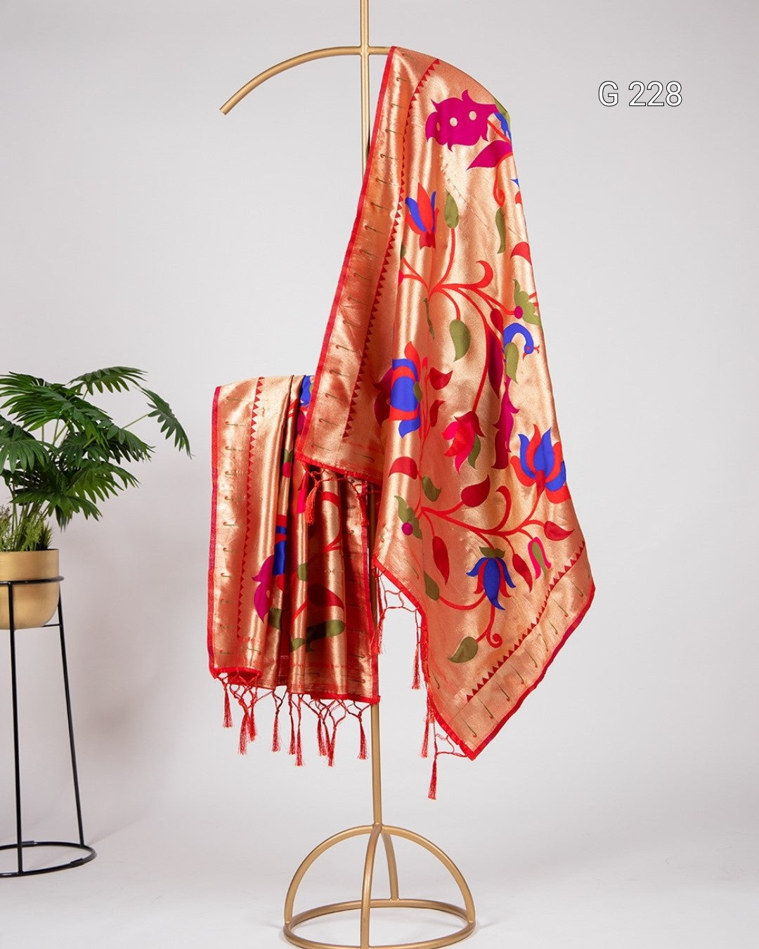 Decorative orange scarf with floral patterns on a gold stand against a white background
