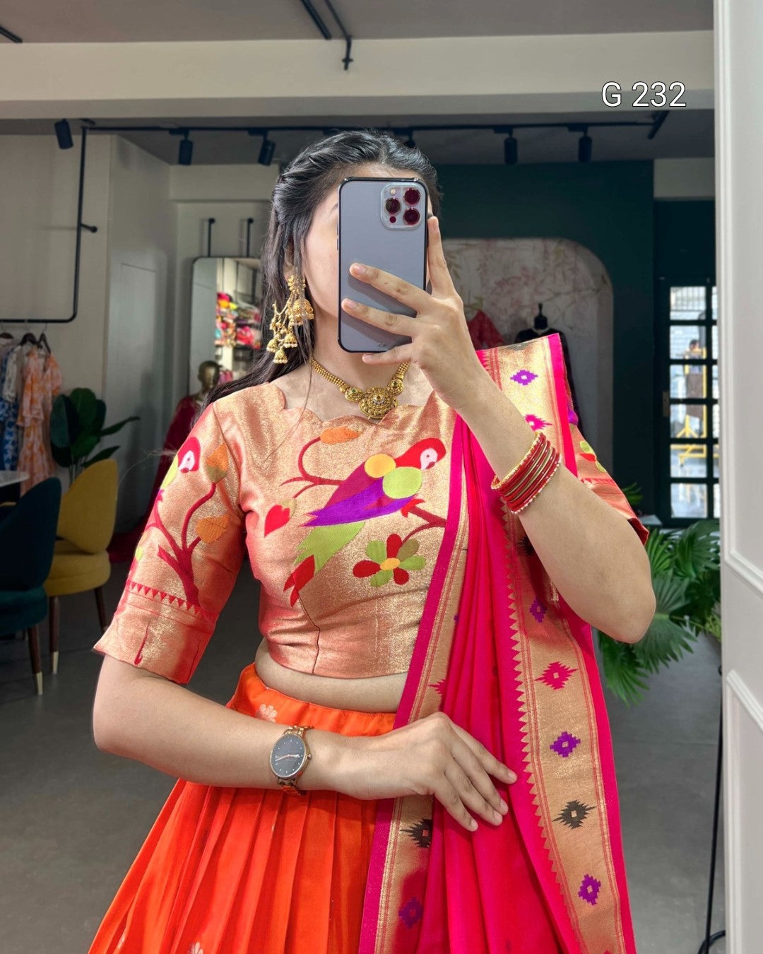 Person wearing a traditional outfit with a colorful blouse and red saree in an indoor setting.
