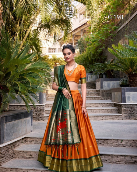 Woman in an orange and green traditional outfit standing outdoors with greenery.