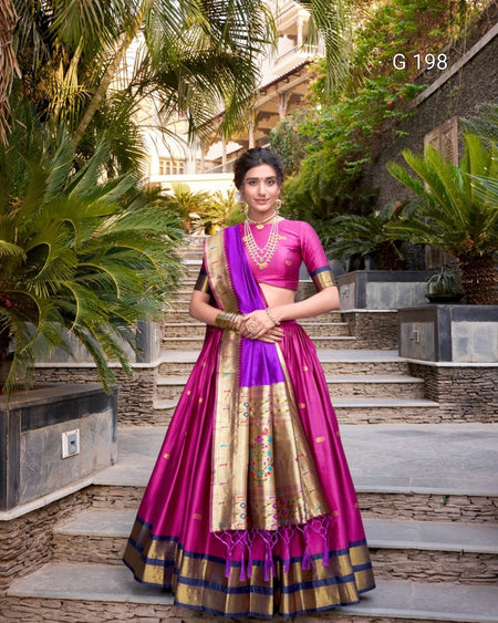 Woman in a traditional purple and gold saree standing outdoors with greenery.