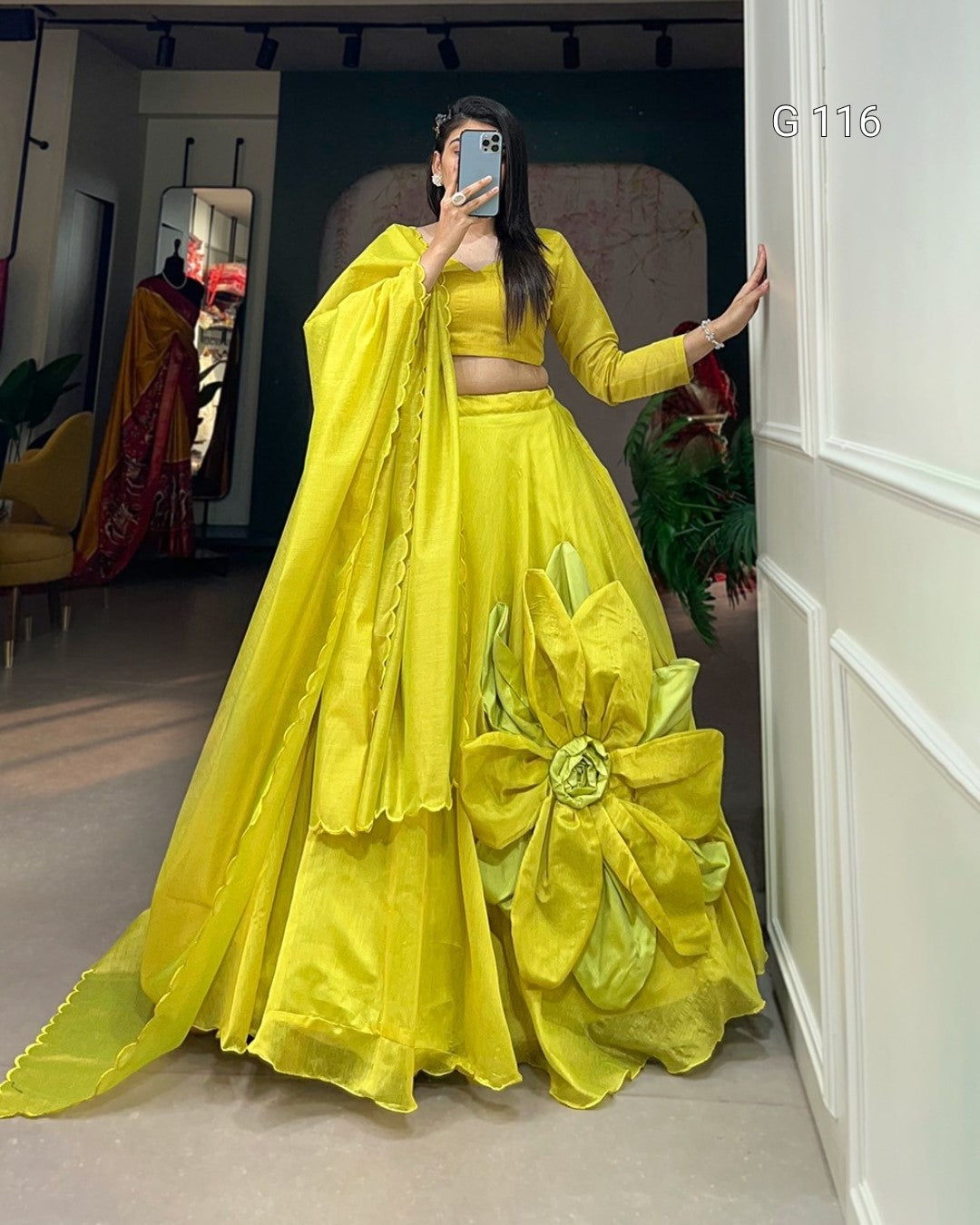 Person wearing a bright yellow traditional outfit with a large flower detail, standing in a room.