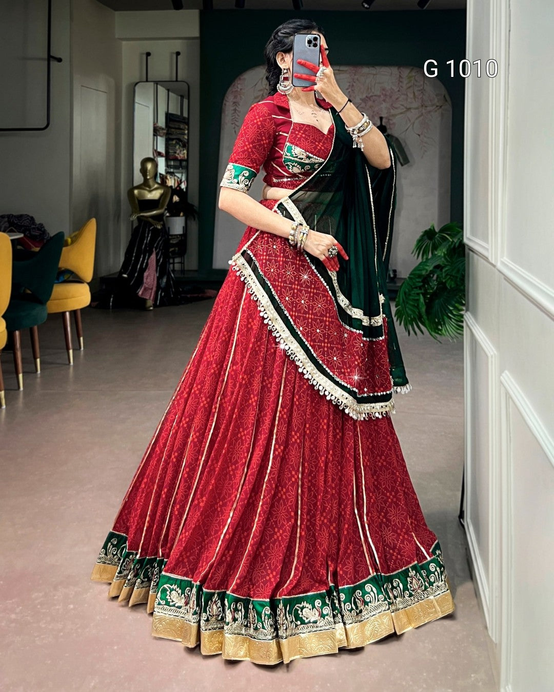 A woman takes a mirror selfie wearing a traditional Indian red velvet lehenga choli with green and gold borders and a dark green dupatta. The text 'G 1010' is visible in the top right corner.