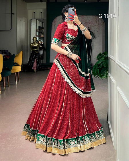 A woman takes a mirror selfie wearing a traditional Indian red velvet lehenga choli with green and gold borders and a dark green dupatta. The text 'G 1010' is visible in the top right corner.