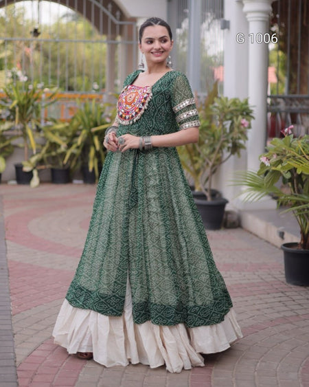 A woman wearing a dark green embroidered Anarkali gown with a cream-colored ruffled underskirt, standing in an outdoor courtyard setting.