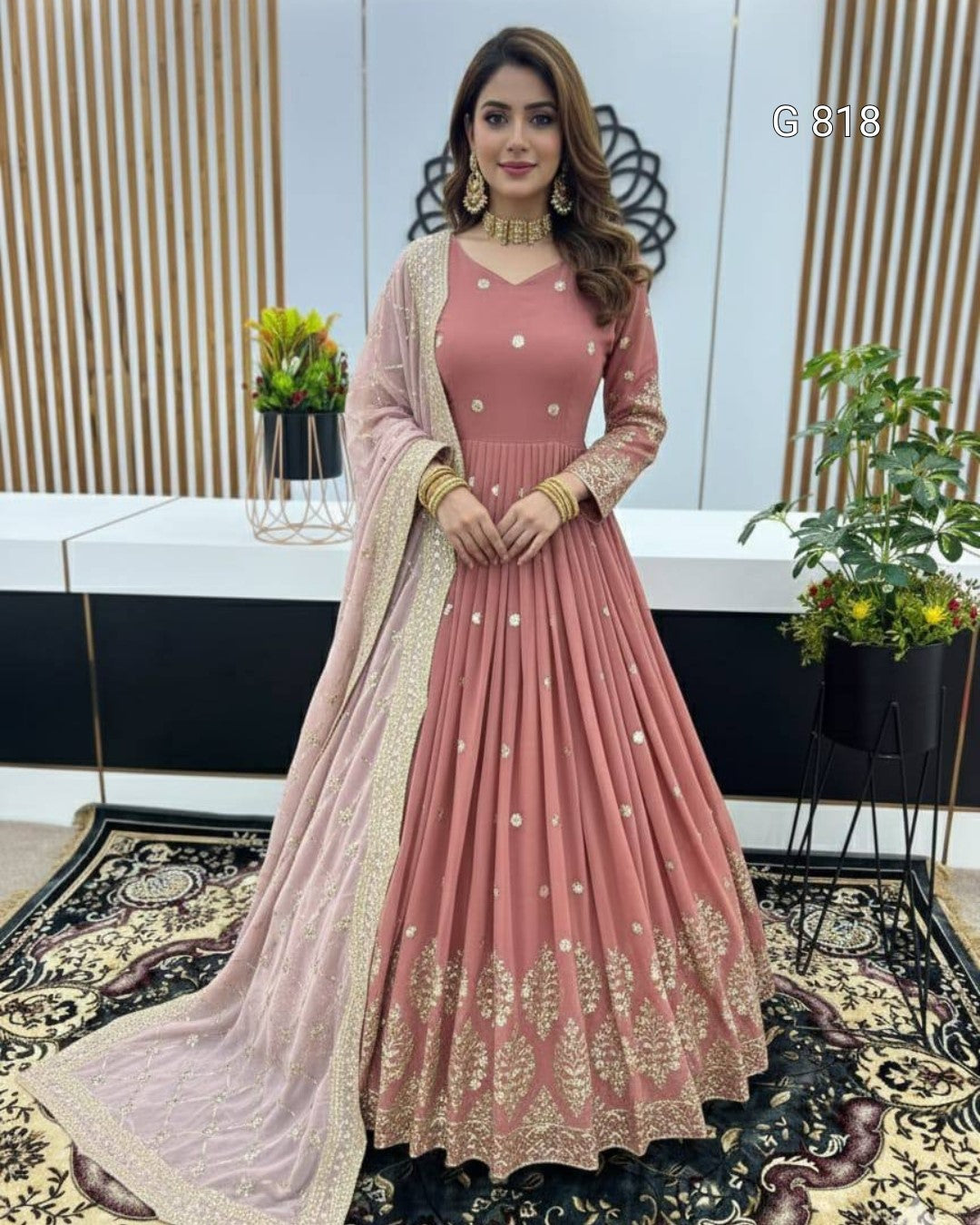 Woman in a pink traditional outfit with gold embroidery in an indoor setting.
