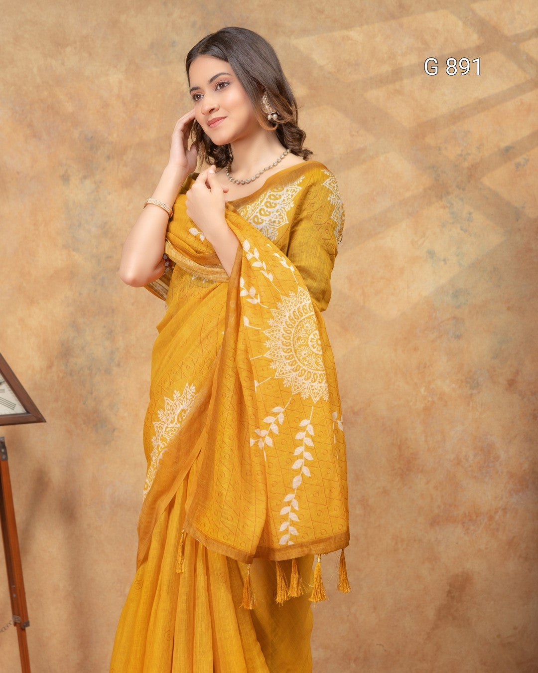 Woman wearing a yellow saree with white patterns against a brown background
