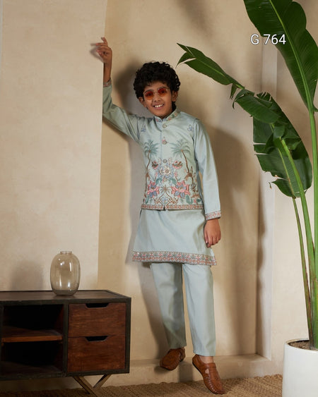 Person wearing a light blue traditional outfit with floral patterns in a room with a wooden cabinet and plant.