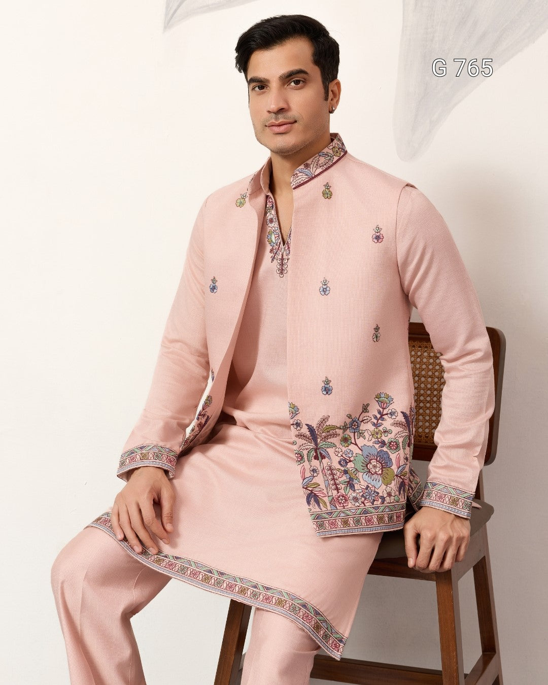 Man wearing a traditional pink embroidered outfit sitting on a chair.