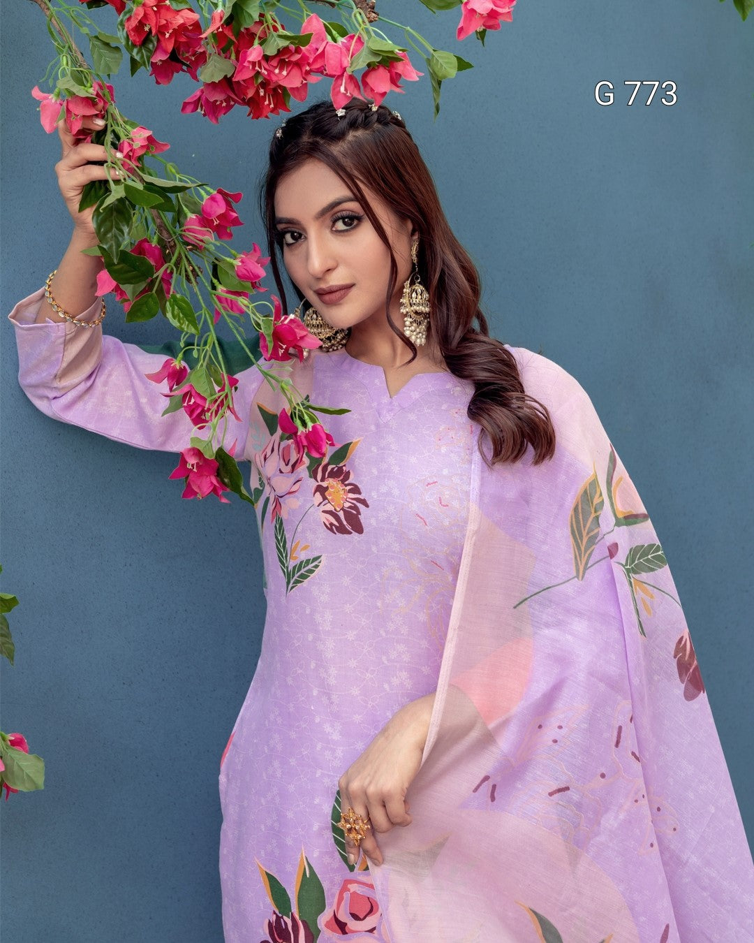 Woman in a light purple floral dress holding pink flowers against a blue background
