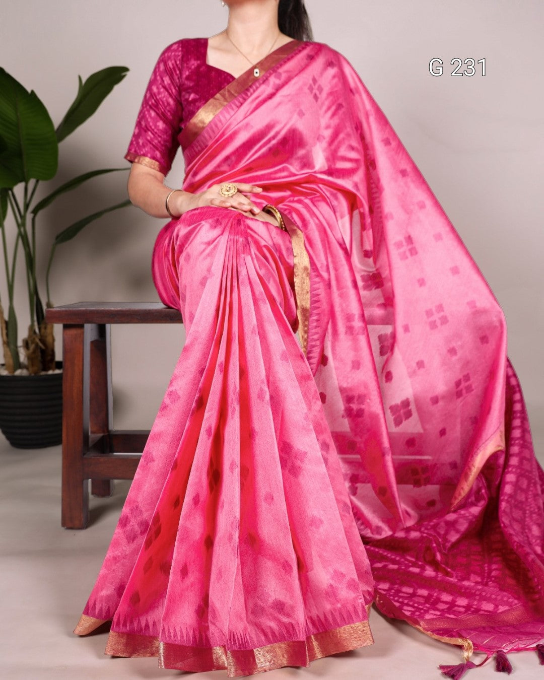 Person wearing a bright pink saree with a subtle pattern, sitting on a chair.