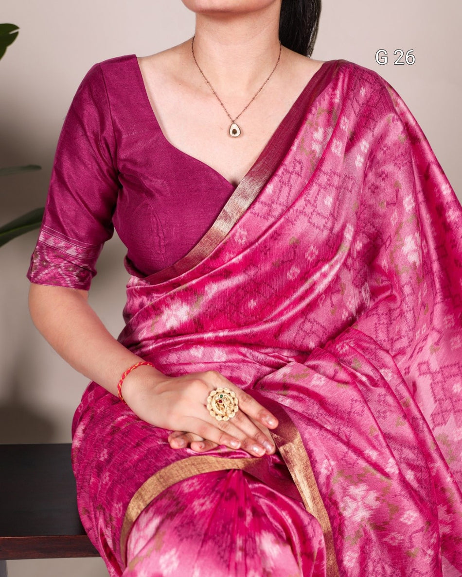Woman wearing a pink saree with a matching blouse, sitting indoors.