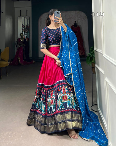 Woman in traditional outfit with blue dupatta and pink skirt, standing indoors.